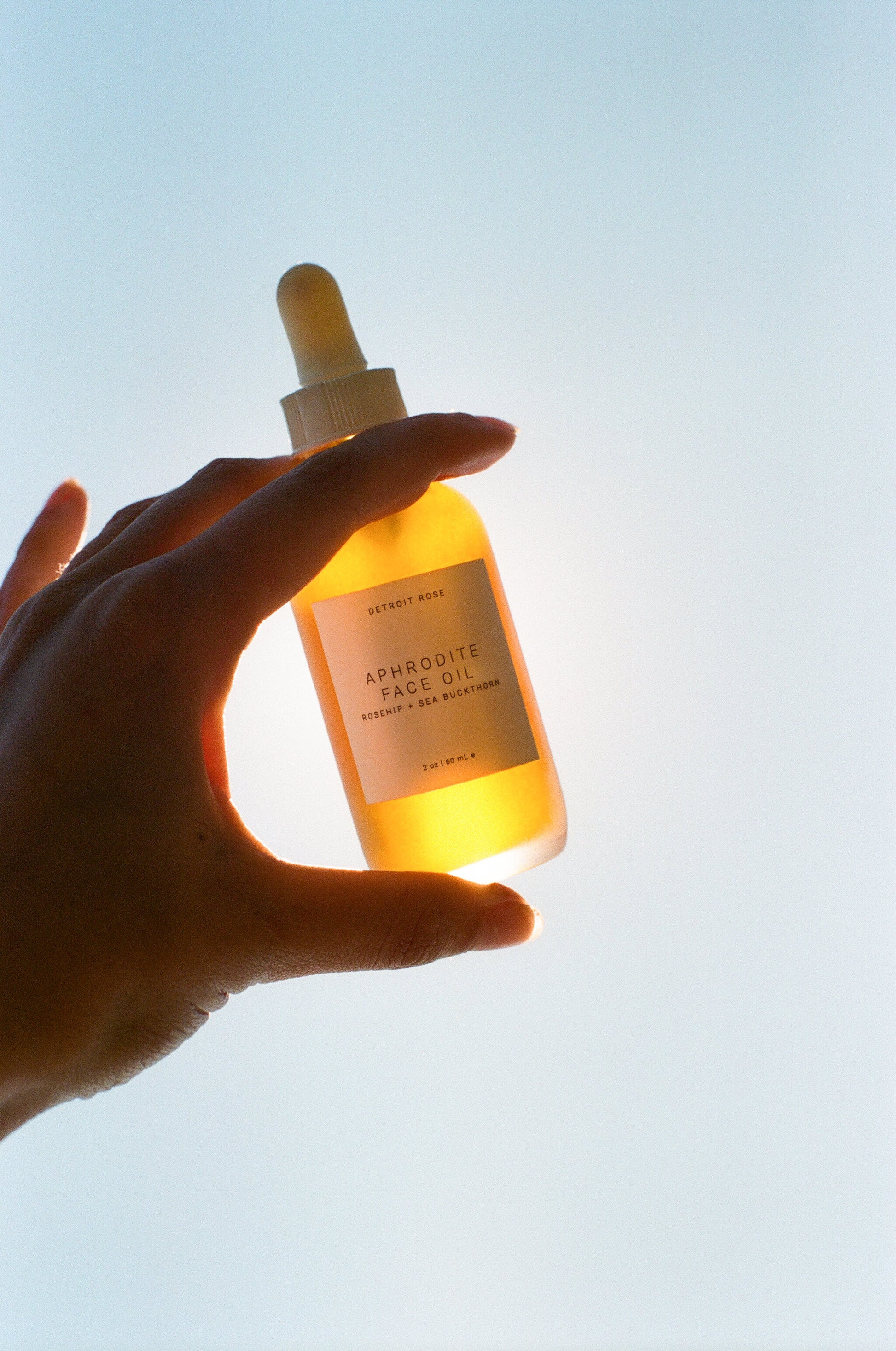 Hand holding a glowing bottle of Aphrodite Face Oil